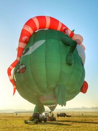 Hot air balloon flying over field against clear sky