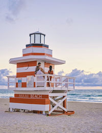 Lighthouse by sea against sky during sunset