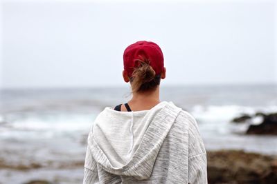 Rear view of woman in cap at beach against sky