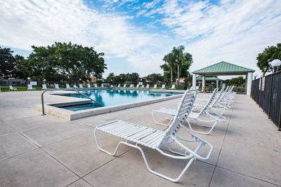 Empty chairs by swimming pool against sky