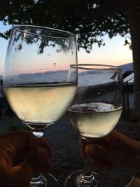 Close-up of hand holding beer glass against sky during sunset