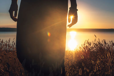 Low section of man standing by sea against sky during sunset