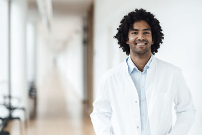 Smiling young male doctor standing at hospital corridor