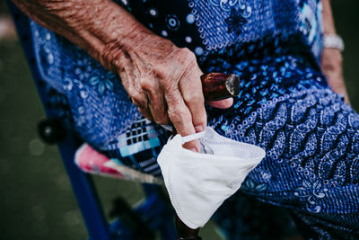 Midsection of senior woman holding mask while sitting over land