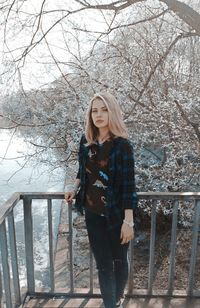 Portrait of young woman standing on bridge against bare trees