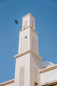 Mosque against blue skies with birds flying around it