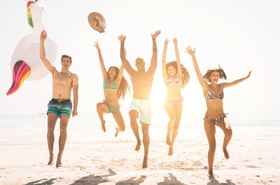 Happy friends jumping on shore of beach against sky