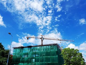 Low angle view of crane by building against blue sky