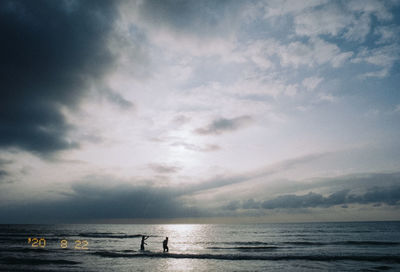 Silhouette people on beach against sky during sunset