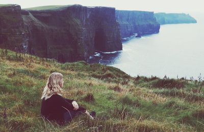 Woman sitting on cliff against sea