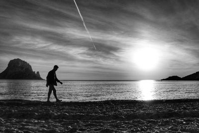 Silhouette man on beach against sky during sunset
