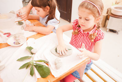 Girls playing with clay and leaf on table at home