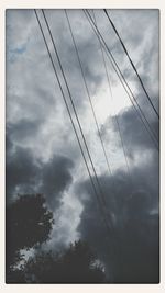 Low angle view of power lines against cloudy sky