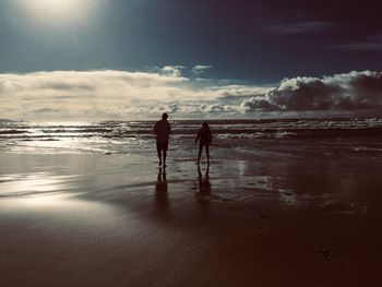 Silhouette men on beach against sky