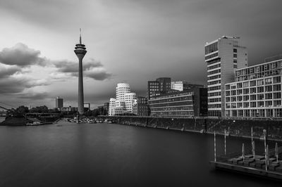 View of modern buildings by river against sky in city