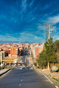 Road amidst buildings in city against blue sky