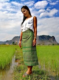 Portrait of young woman standing on field against sky