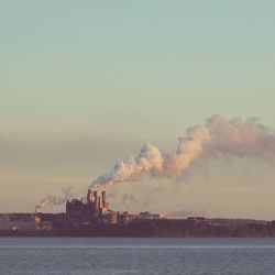 Smoke emerging from chimney at distance with waterfront