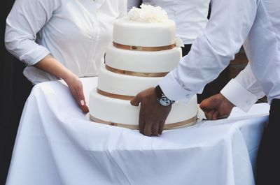 Midsection of waiters placing wedding cake on table in ceremony