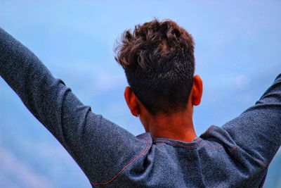 Rear view of man with arms raised standing against sky