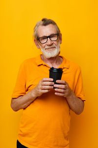 Portrait of young woman using mobile phone against yellow background