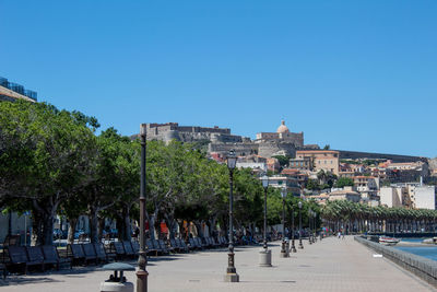 Road by trees and buildings against clear blue sky