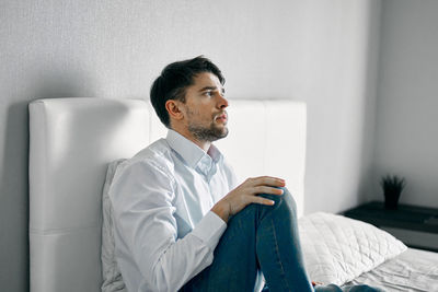 Young man looking away while sitting on sofa at home