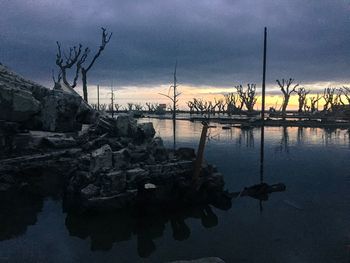 Reflection of silhouette trees on water against sky