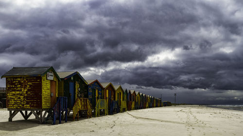 Hooded chairs on beach against cloudy sky