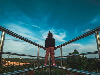 Rear view of girl standing on railing against sky