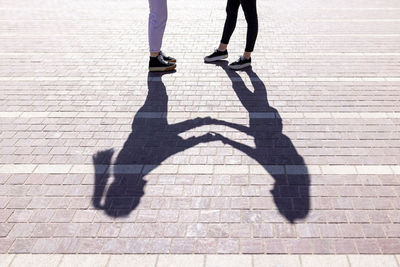 Shadow of female friends with holding hands standing on footpath during sunny day
