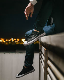 Low section of man sitting on railing at night