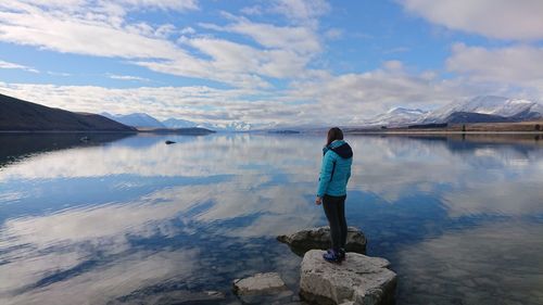 Full length of woman standing by lake against cloudy sky during winter