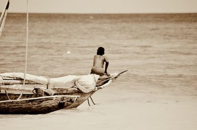 Full length of shirtless man sitting on beach against sky