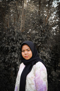 Portrait of a beautiful young woman standing against trees