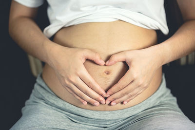 Midsection of pregnant woman making heart shape on belly