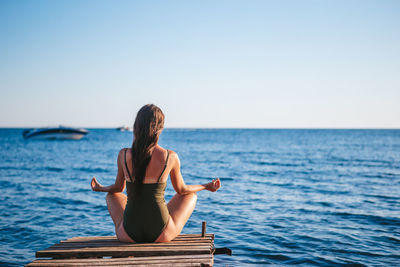 Woman sitting by sea against clear sky