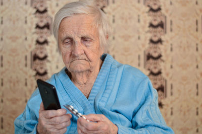 Portrait of a 90-year-old sick pensioner who holds a package of pills and a phone in her hands.