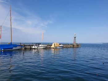 Sailboats moored in sea against blue sky