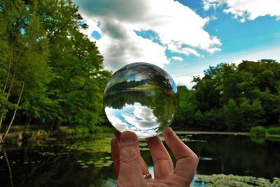 Close-up of hand holding crystal ball with reflection of trees, lake and sky in dulwich park, london