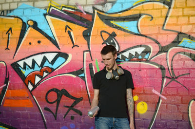 Full length of young man standing against graffiti wall