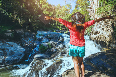 Rear view of woman standing on rock against waterfall