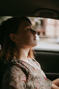 Portrait of beautiful young woman with dark short hair and silver earrings sitting in the car window