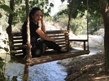 Portrait of smiling woman sitting on swing in forest