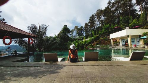 Rear view of woman by swimming pool against sky