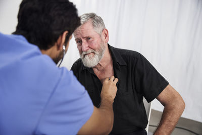 Male doctor examining senior patient with stethoscope