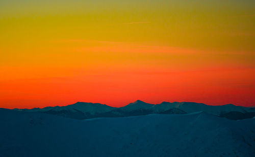 Scenic view of snowcapped mountains against dramatic sky during sunset