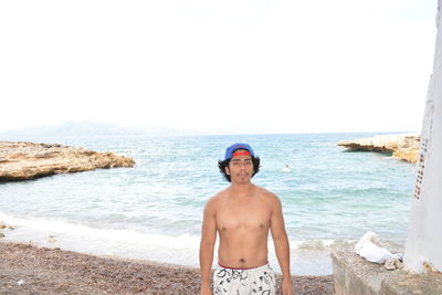 Portrait of shirtless man standing on beach against clear sky