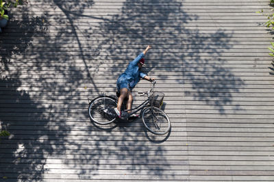 High angle view of woman with bicycle lying down on wooden walkway