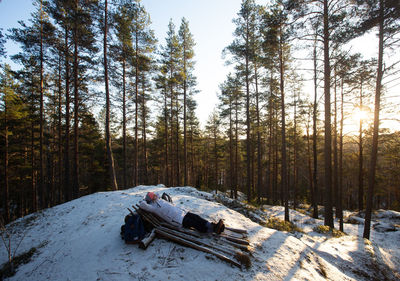 Woman lying on snow covered hill against trees in forest